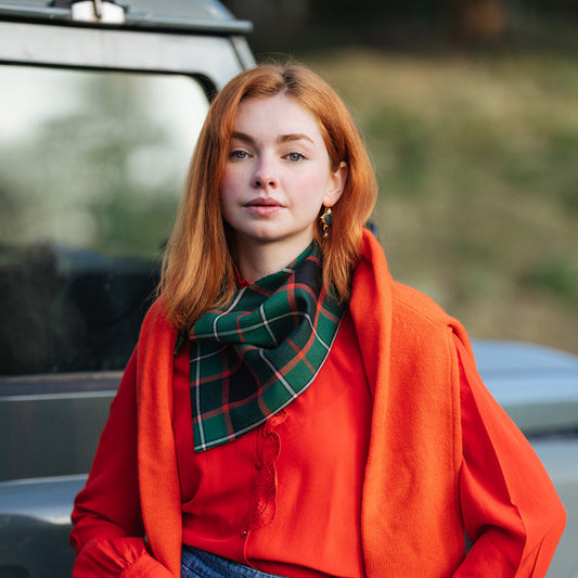 Person wearing a bright red jacket and plaid scarf standing in front of a vehicle.