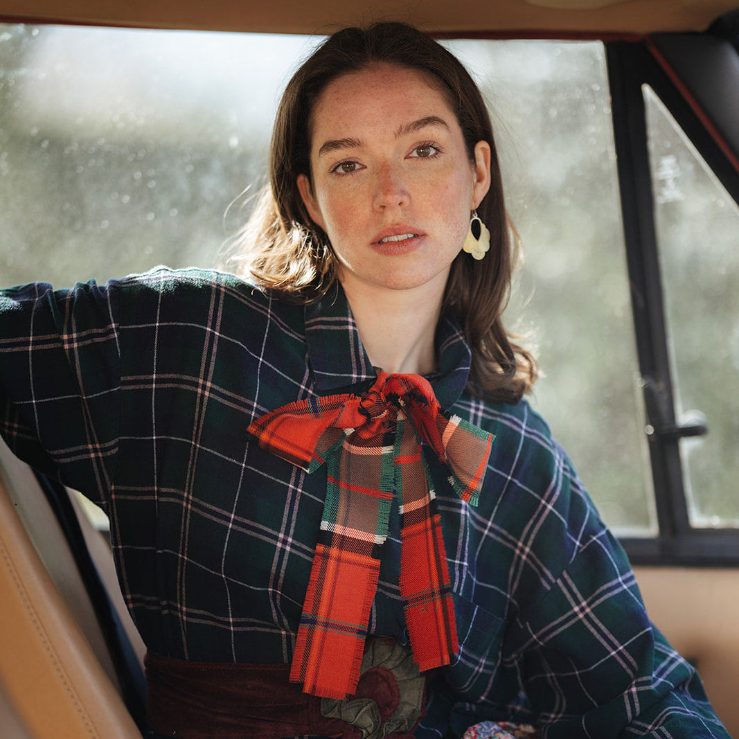 Woman sitting inside a vehicle wearing a plaid coat with a red tartan scarf.