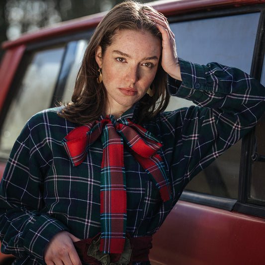 Woman in a plaid outfit with a red scarf standing next to a red vintage landrover.