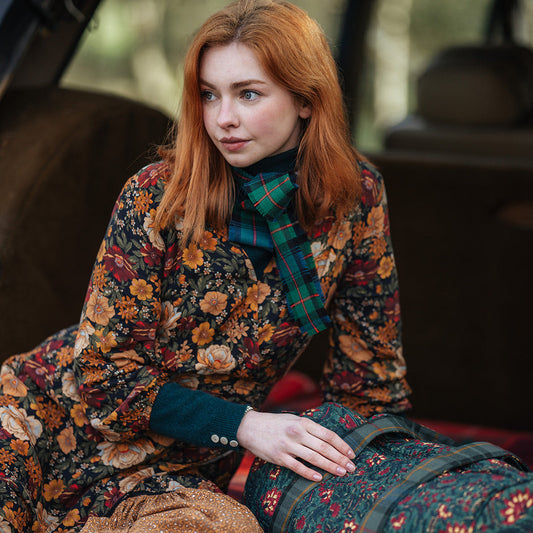 Woman with red hair sitting inside classic rangerover with a floral patterned dress and weekend bag.