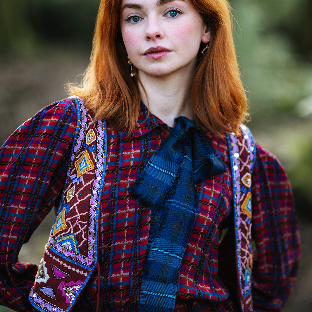 Woman wearing a plaid dress with a colorful patterned jacket outdoors